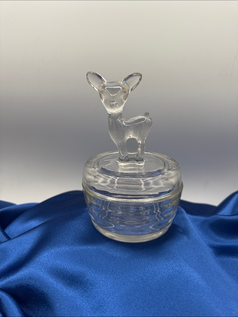 This piece is a vintage clear glass deer fawn powder jar manufactured by the Jea